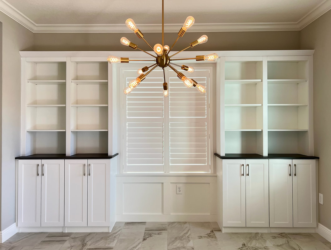 Custom white built-in bookcase wall with dark countertops and sputnik chandelier